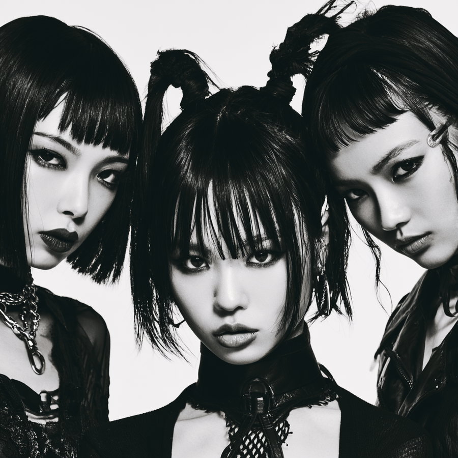 Black and white photograph of three women with distinct edgy hairstyles and makeup, looking directly at the camera, wearing dark clothing and chains