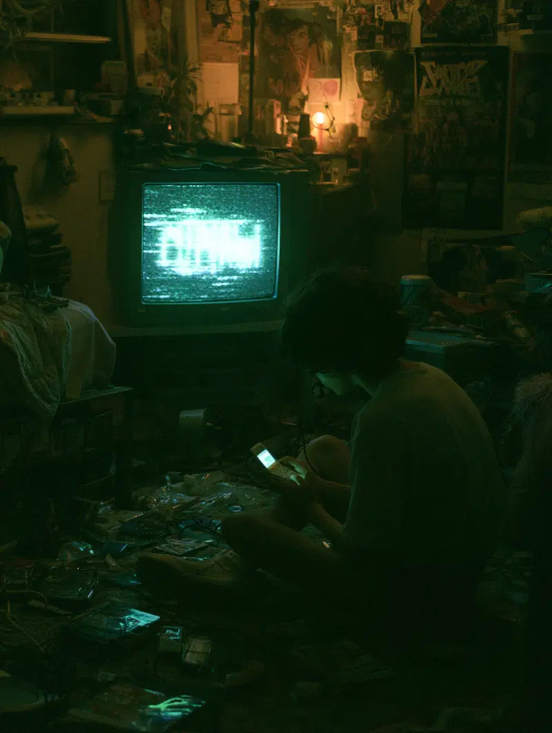 Person sitting on floor in dark room glowing from phone and glitchy TV