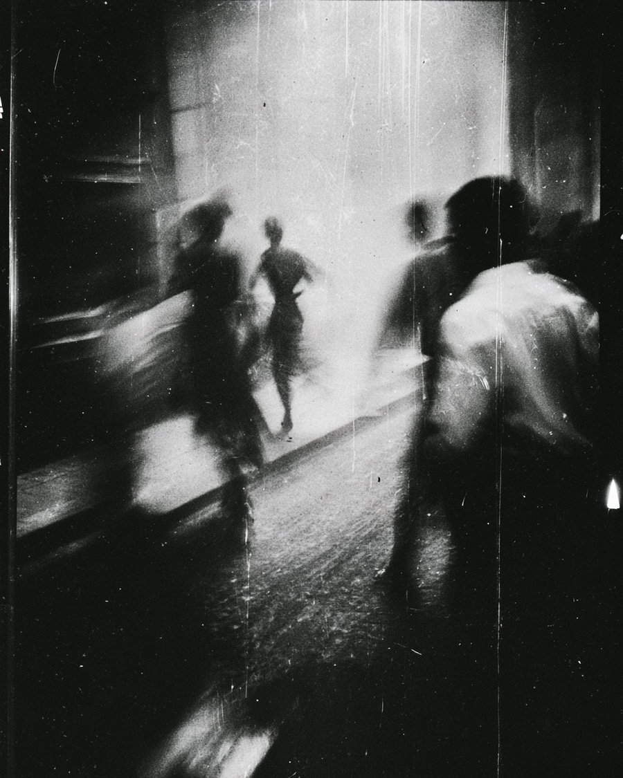 Black and white abstract photo showing blurred silhouettes of people walking in a grainy and textured environment