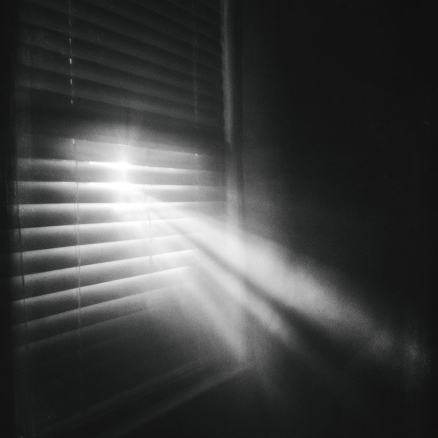 A beam of light coming through partially opened window blinds illuminating the dark interior