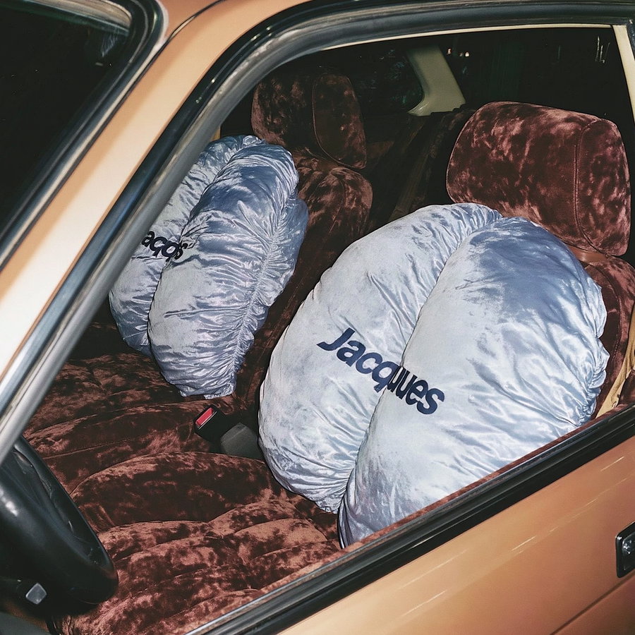 Inside view of a car showing plush brown seats and large shiny silver cushions with 'Jacques' text on them