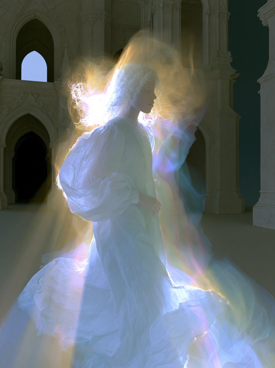 A glowing ethereal figure with white flowing hair and a billowing white dress stands in a gothic cathedral with high arches, illuminated by radiant, multicolored light effects surrounding the figure.