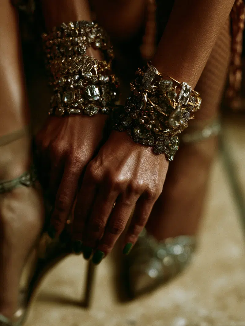 Close-up photograph of hands adorned with ornate jeweled bracelets and green nail polish