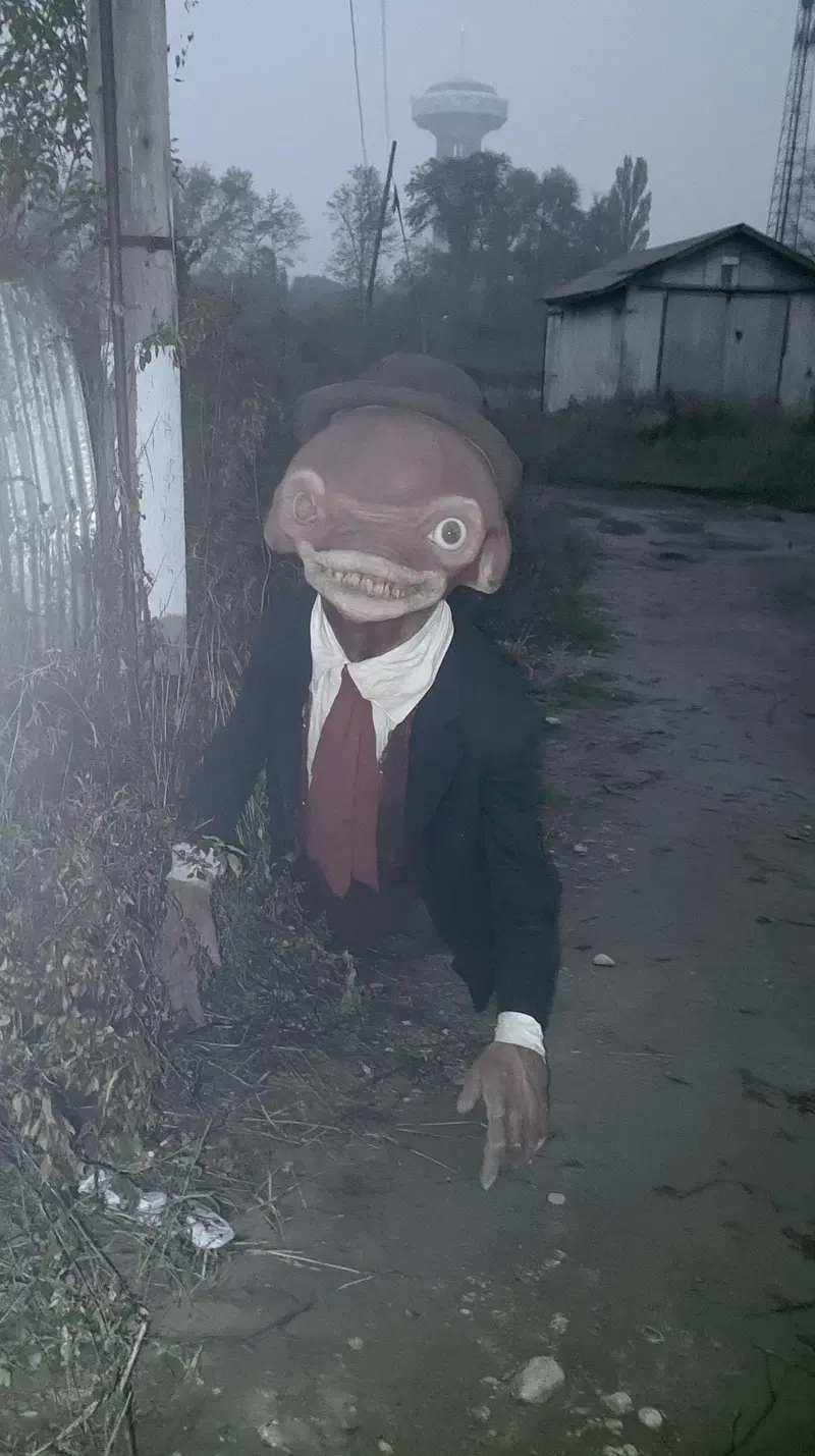 Eerie humanoid creature crawling on a misty rural path near old buildings