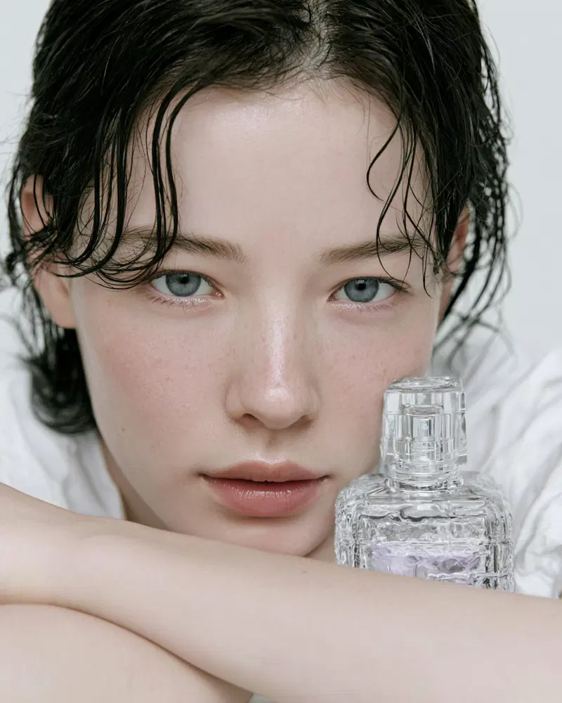 Close-up portrait of a young woman with wet hair holding a clear perfume bottle