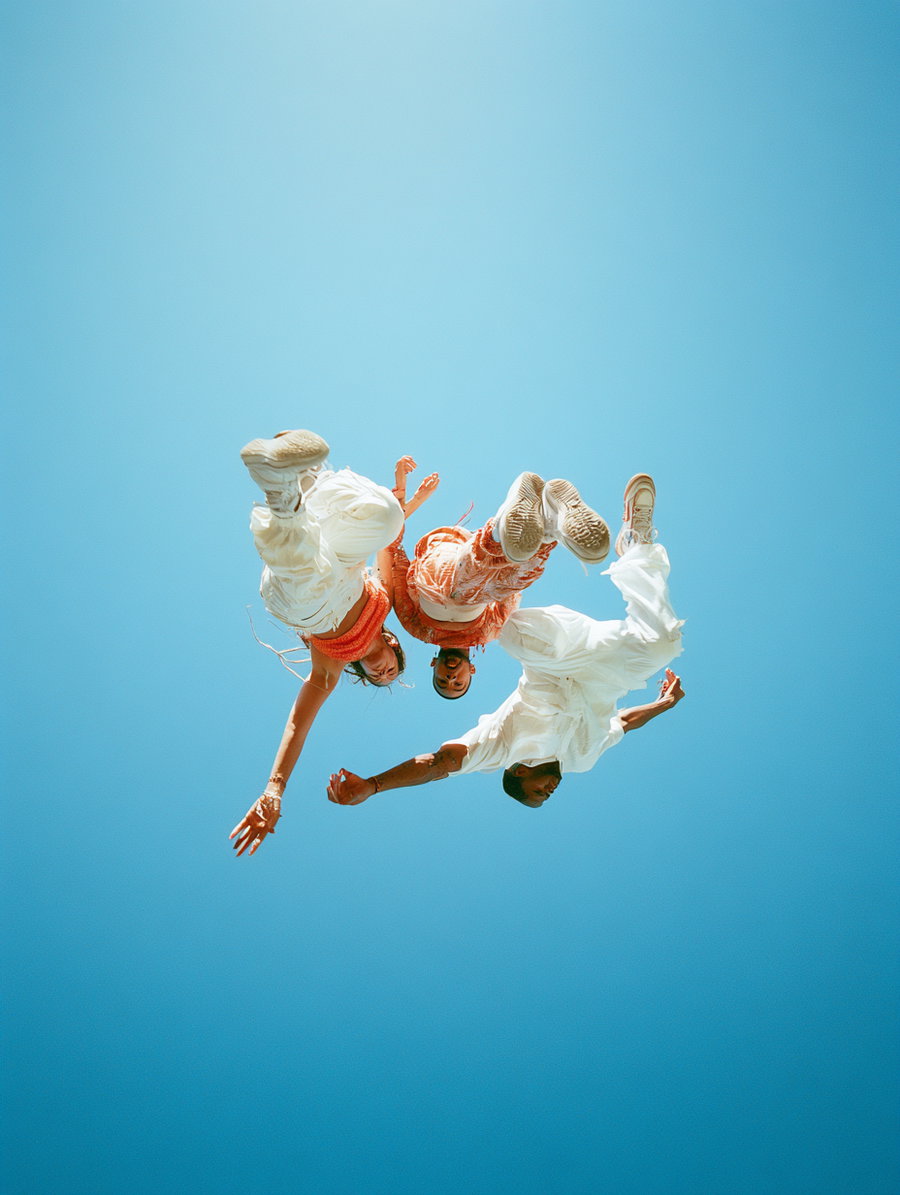 Three people dressed in white and orange clothes jumping in the air captured from below with clear blue sky background