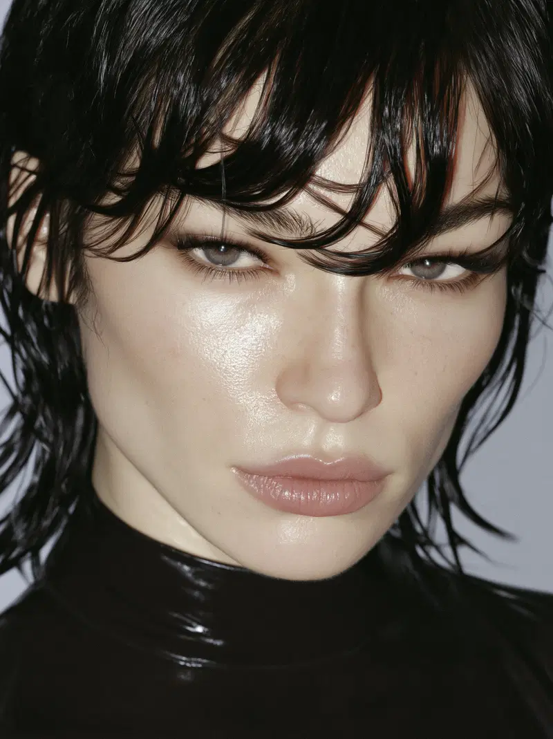 Close-up portrait of a person with wet hair and glossy skin in a dark turtleneck