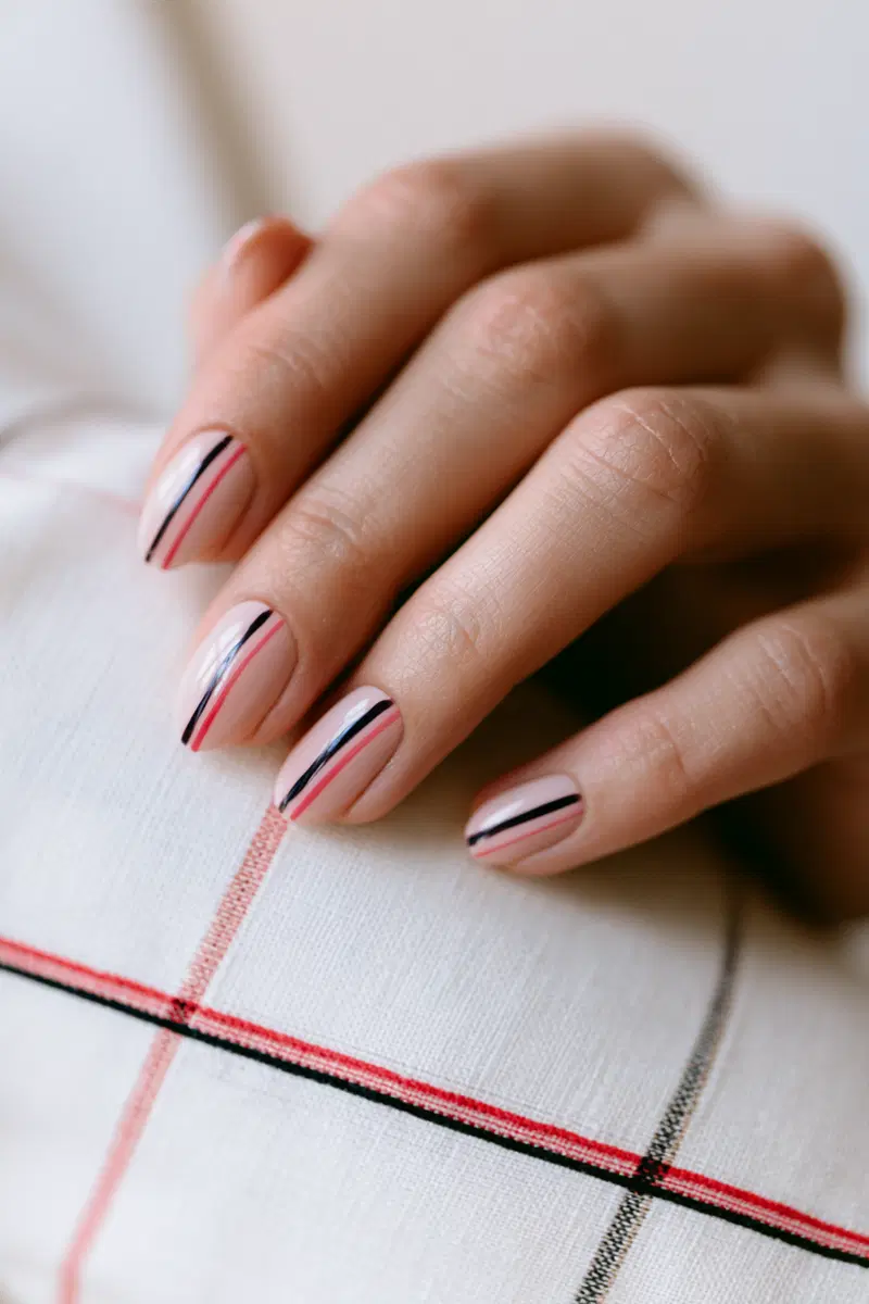 Close-up of hand with minimalist nail art featuring black and red vertical stripes