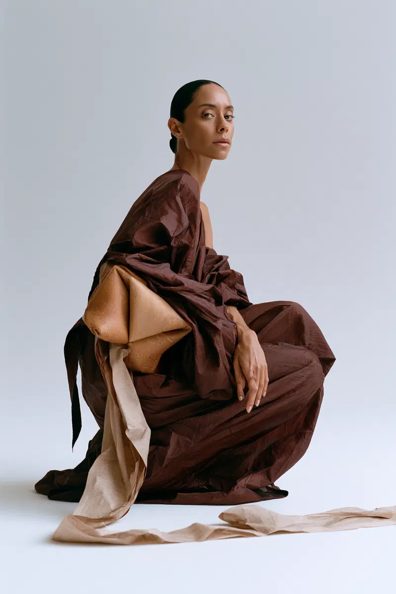 Minimalist portrait of a woman in a draped brown dress with fabric details