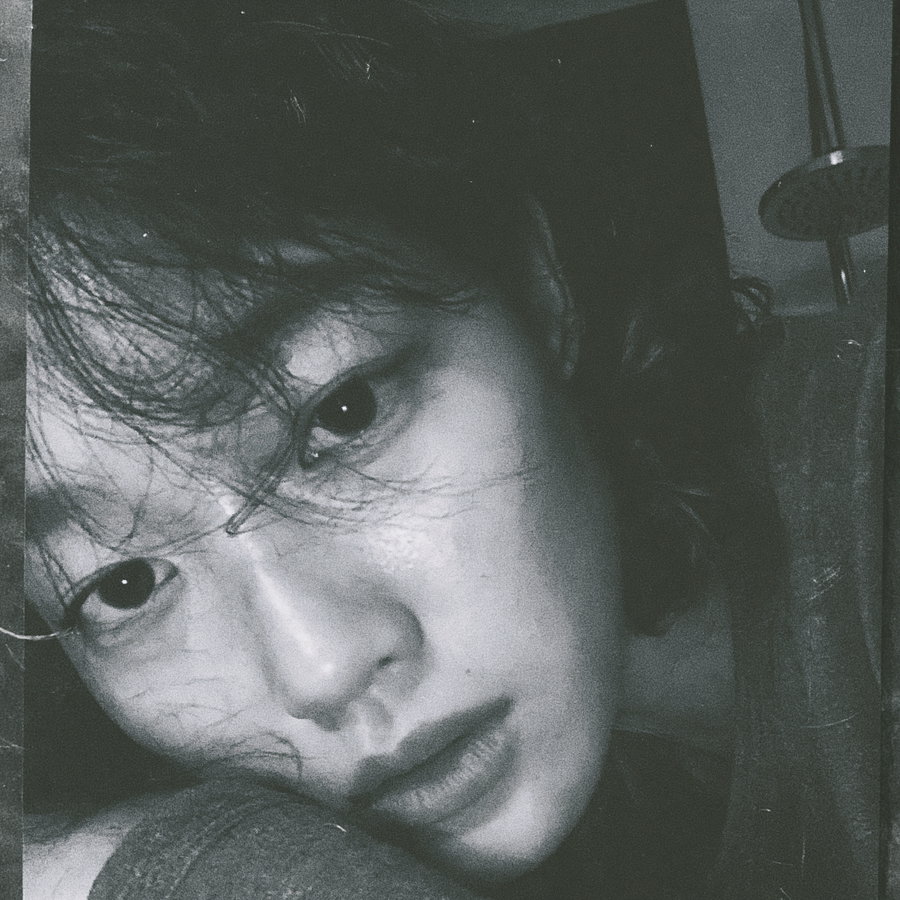 Black and white close-up photo of a person's face lying on their arm with loose hair strands partially covering the eyes