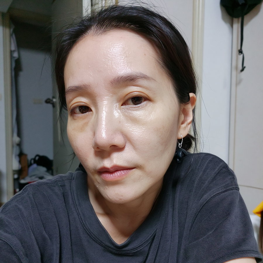 Close-up image of a woman with dark hair pulled back, wearing a dark shirt and black earrings, in an indoor setting with a door and some objects in the background