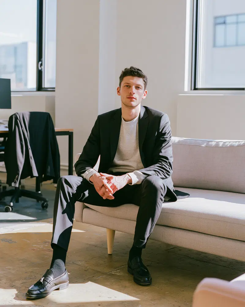 Young man in formal attire sitting on a beige couch in modern office