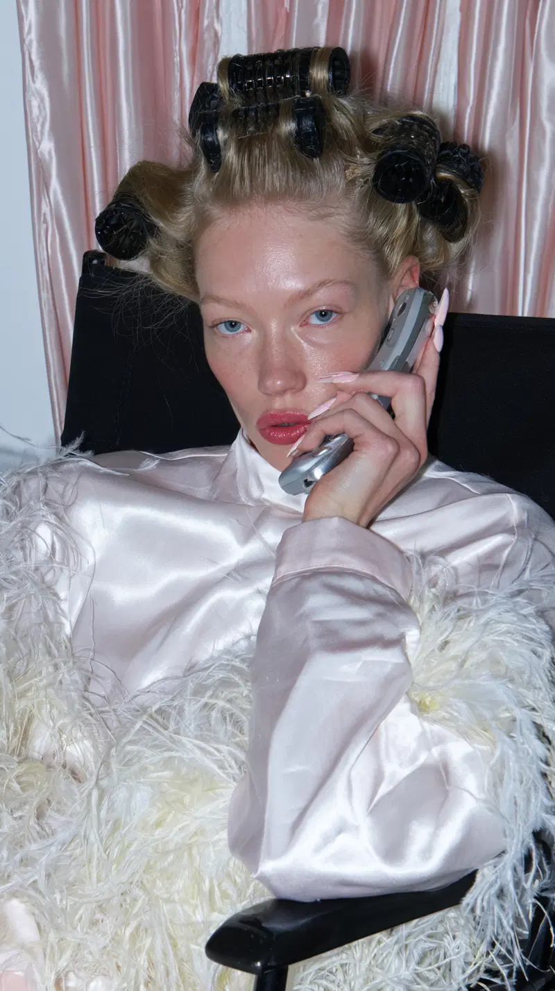 Woman in satin and feathered outfit with hair rollers on phone call