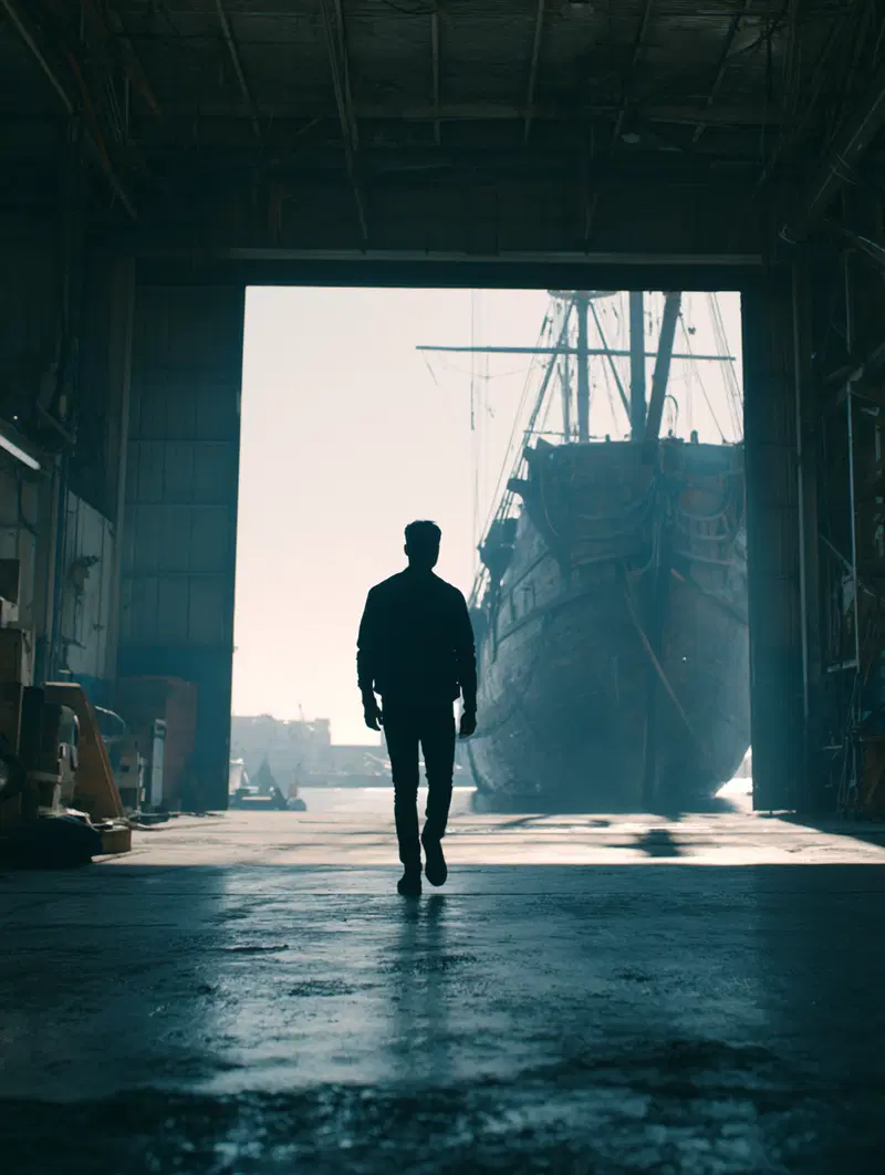 Silhouette of a man walking towards a large docked ship inside a warehouse