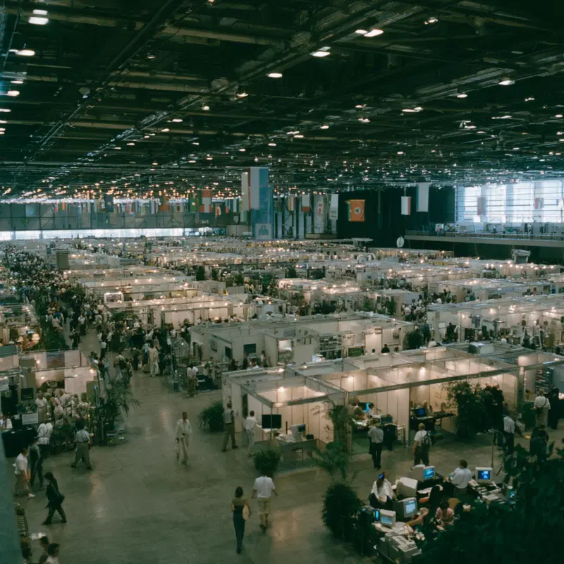 Large indoor exhibition hall with multiple booths and visitors walking around