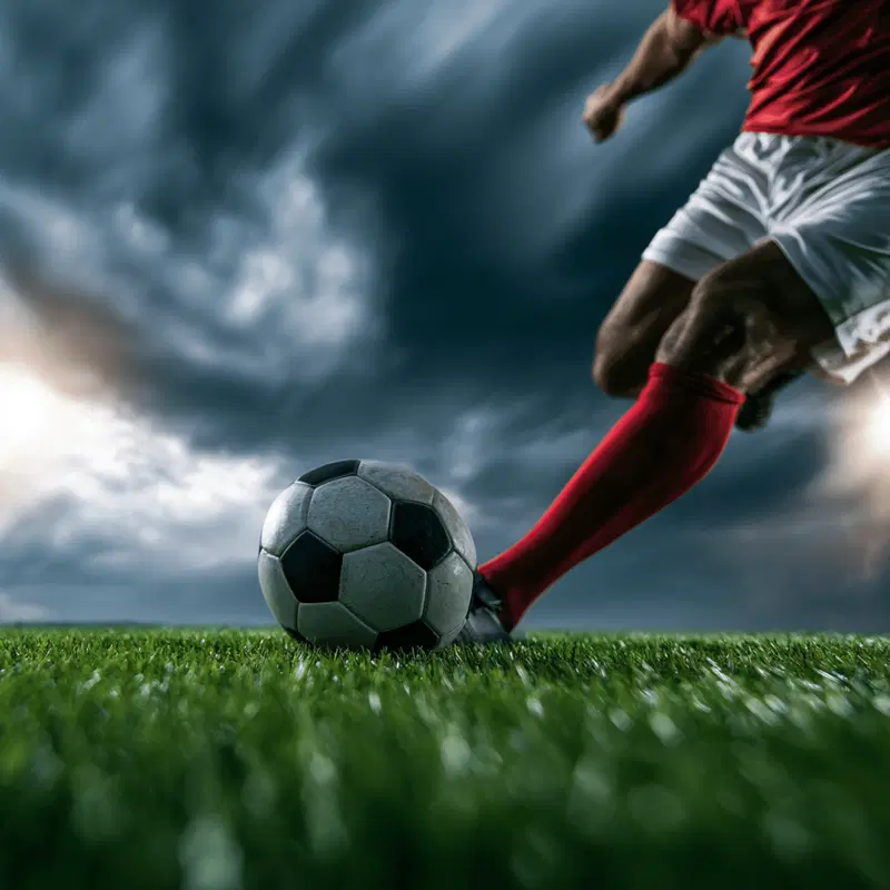 Dynamic close-up of soccer player kicking ball on green field under dramatic sky
