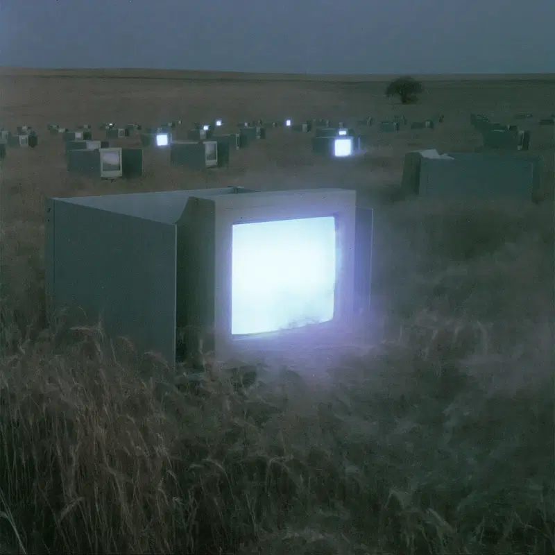 Surreal landscape with glowing vintage televisions in a misty field at dusk