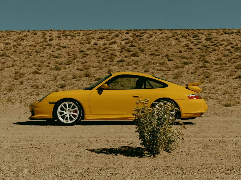 Yellow vintage sports car parked on a dusty desert road with clear sky