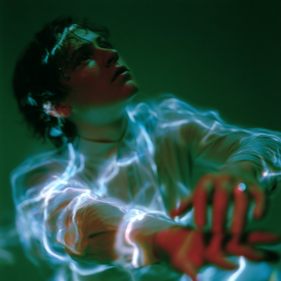 A close-up of a person looking upwards with glowing blue light streaks swirling around their upper body and arms, set against a dark green background