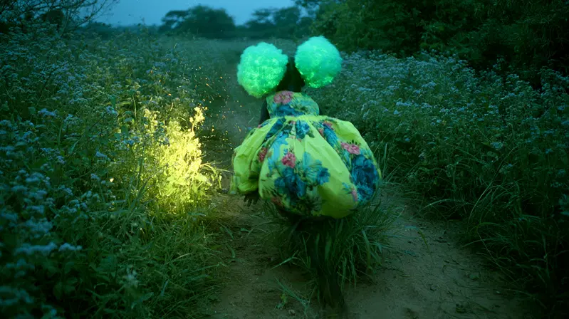 Person wearing a bright floral puff dress and glowing accessories in a dreamy path