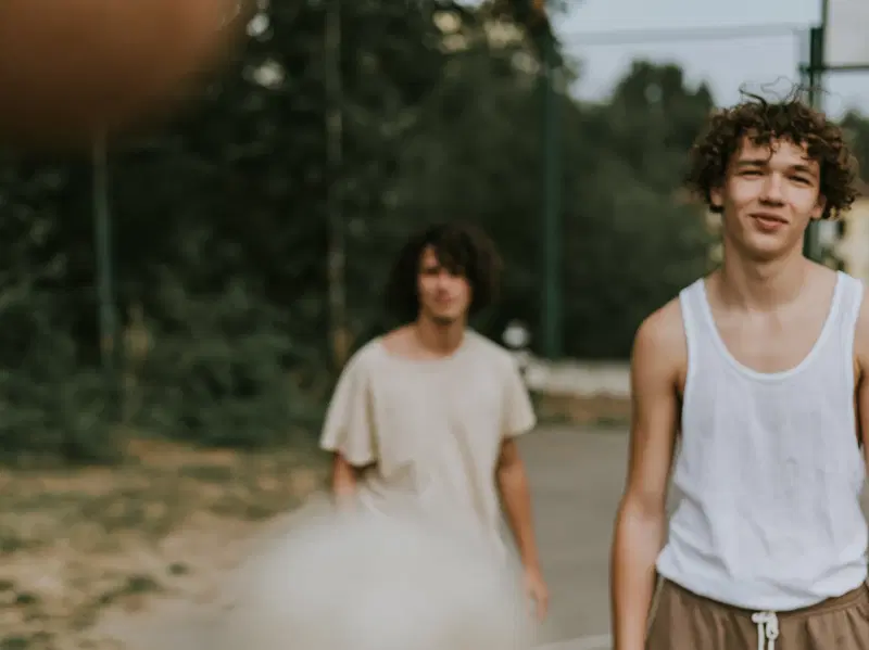 Two young men standing outdoors on a sports court with greenery in the background