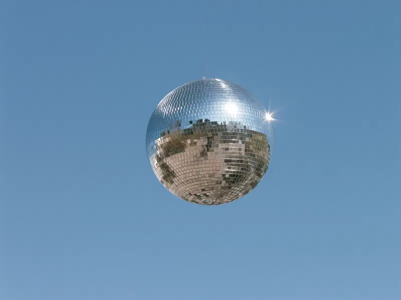 Reflective silver disco ball hanging against clear blue sky background