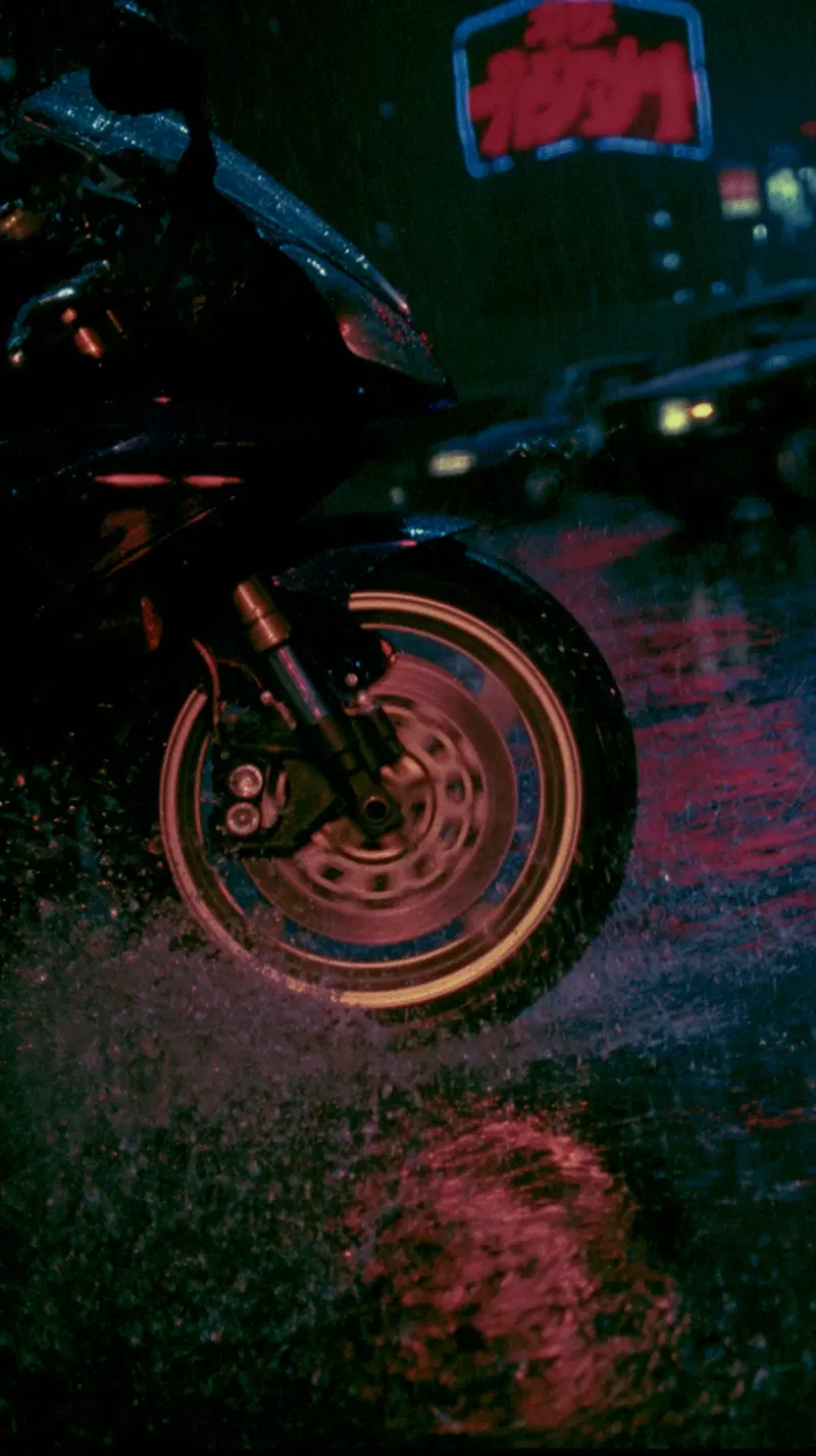 Close-up of a motorcycle wheel splashing through water on a rainy night city street