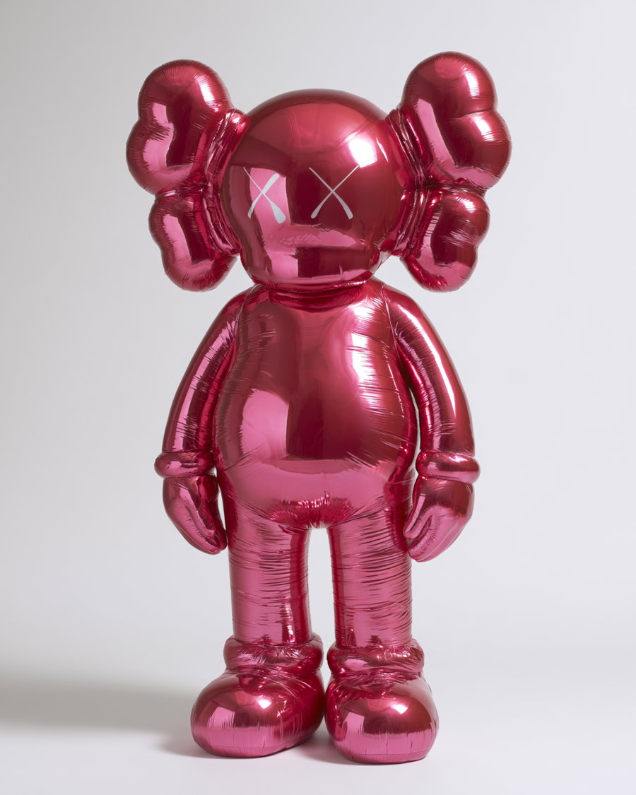 A red metallic balloon sculpture shaped like a cartoon character with large ears and crossed out eyes standing against a plain light background