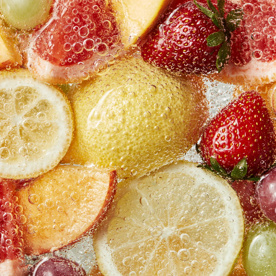 Slices of lemon, grapefruit, apple, whole strawberries and grapes underwater with numerous bubbles surrounding them