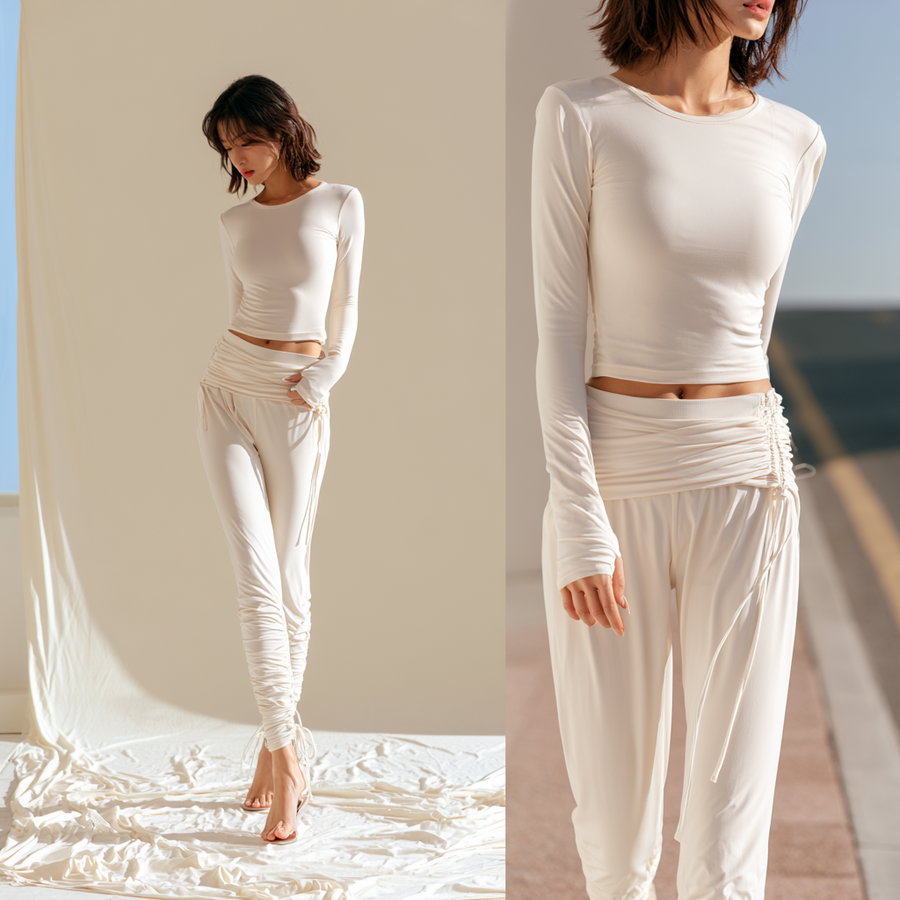 Woman wearing a white long-sleeve fitted top and ruched white pants with adjustable drawstrings, standing barefoot on a white cloth backdrop indoors