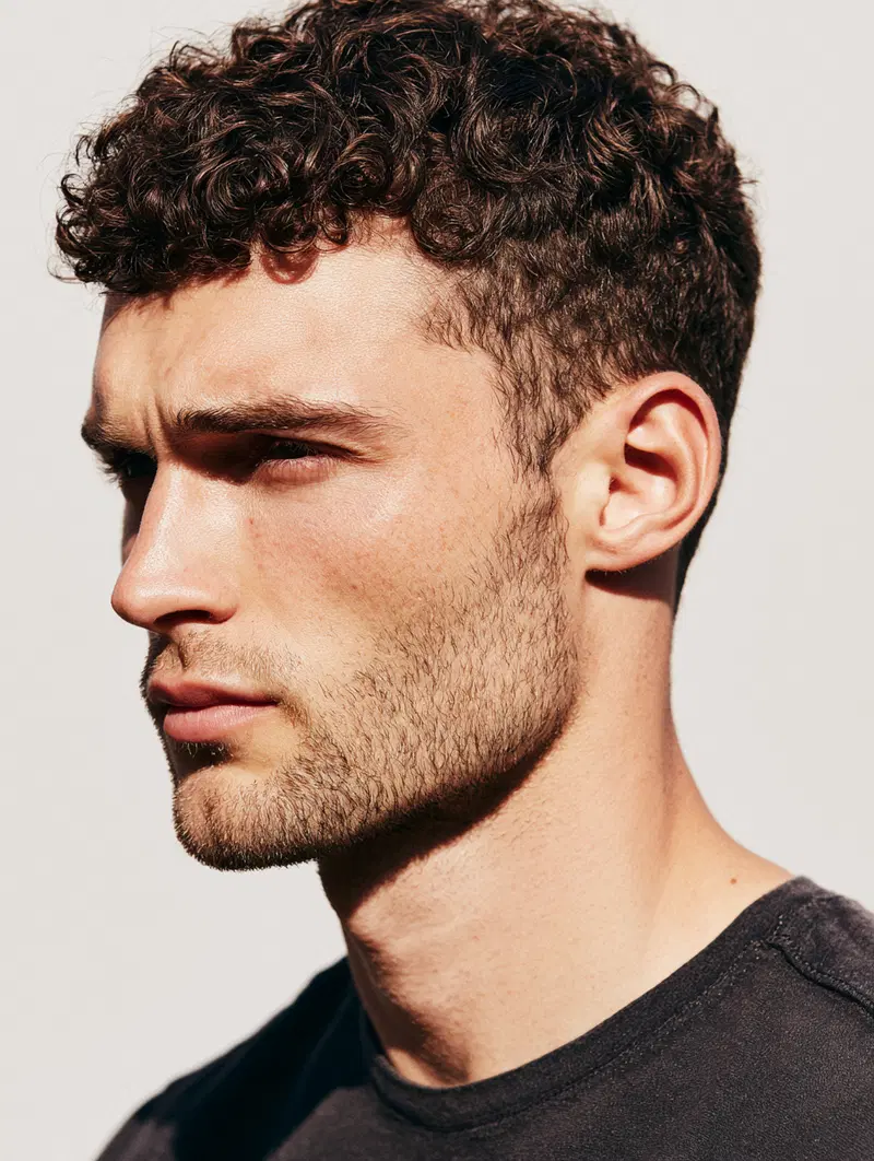 Portrait of a young man with curly hair and a short beard in natural light