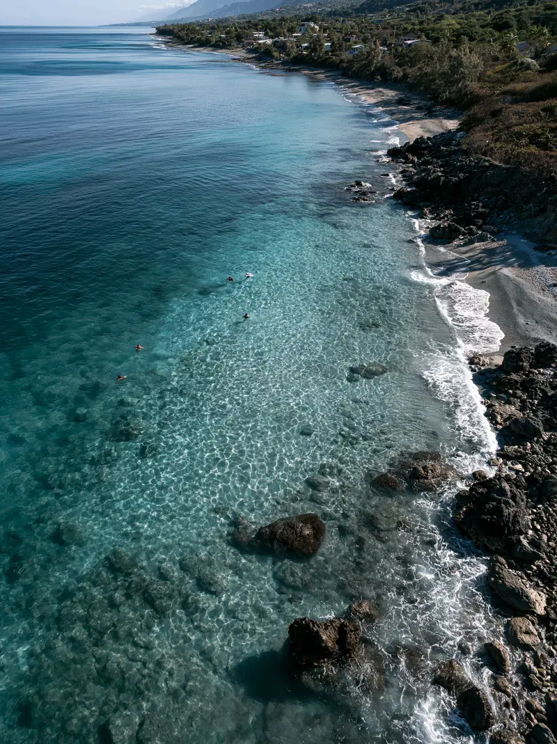 Aerial view of crystal clear waters and rocky coastline with swimmers