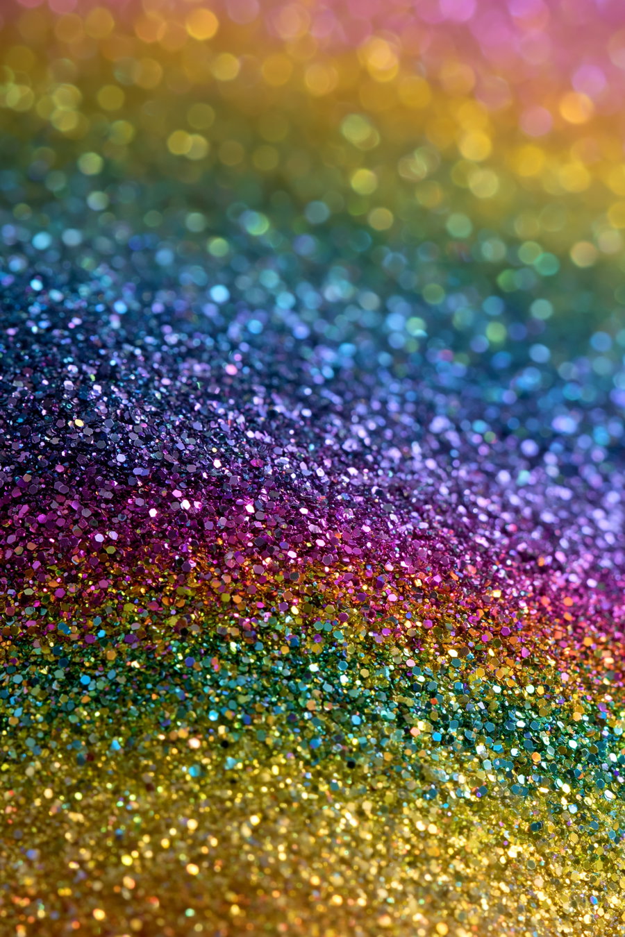 A close-up image showing a surface covered in shining multicolored glitter particles, displaying colors like gold, green, pink, purple, and blue with blurred circular bokeh lights in the background.