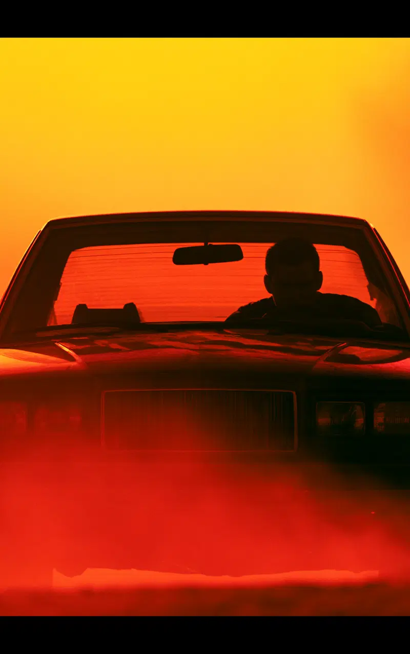Silhouetted driver in a classic car against a fiery sunset