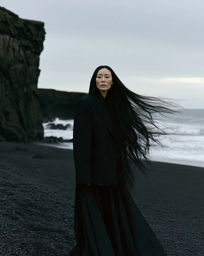 Woman in long black coat and flowing hair on a rocky black beach