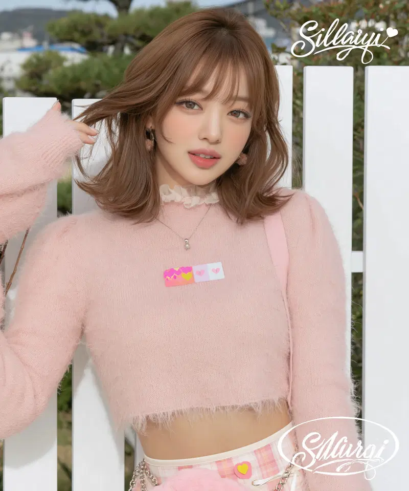 Young woman in pastel pink outfit posing against white fence outdoors
