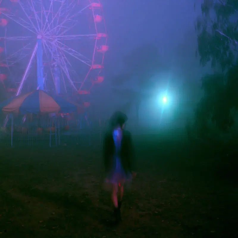 Silhouetted figure in a foggy night with an eerie ferris wheel