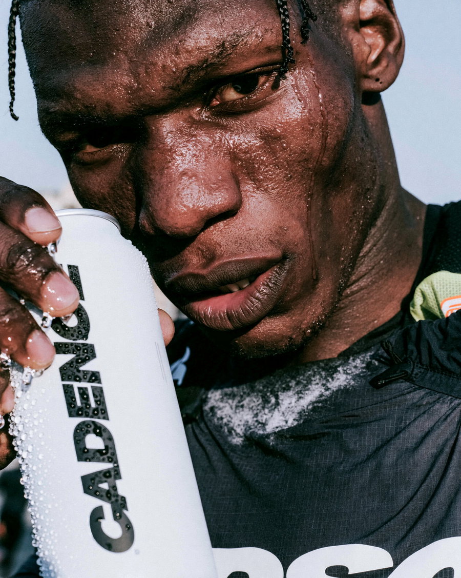 A close-up portrait of a male athlete holding a water can, displaying sweat and determination.