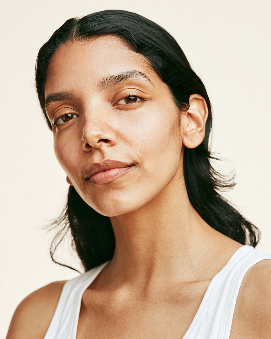 A close-up portrait of a woman with long dark hair and subtle makeup, looking confidently at the camera against a soft, neutral background.
