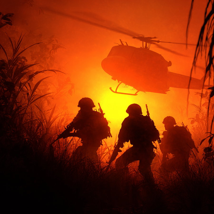 Silhouetted soldiers carrying rifles walking through thick jungle foliage with an orange-red glowing background and a helicopter flying above