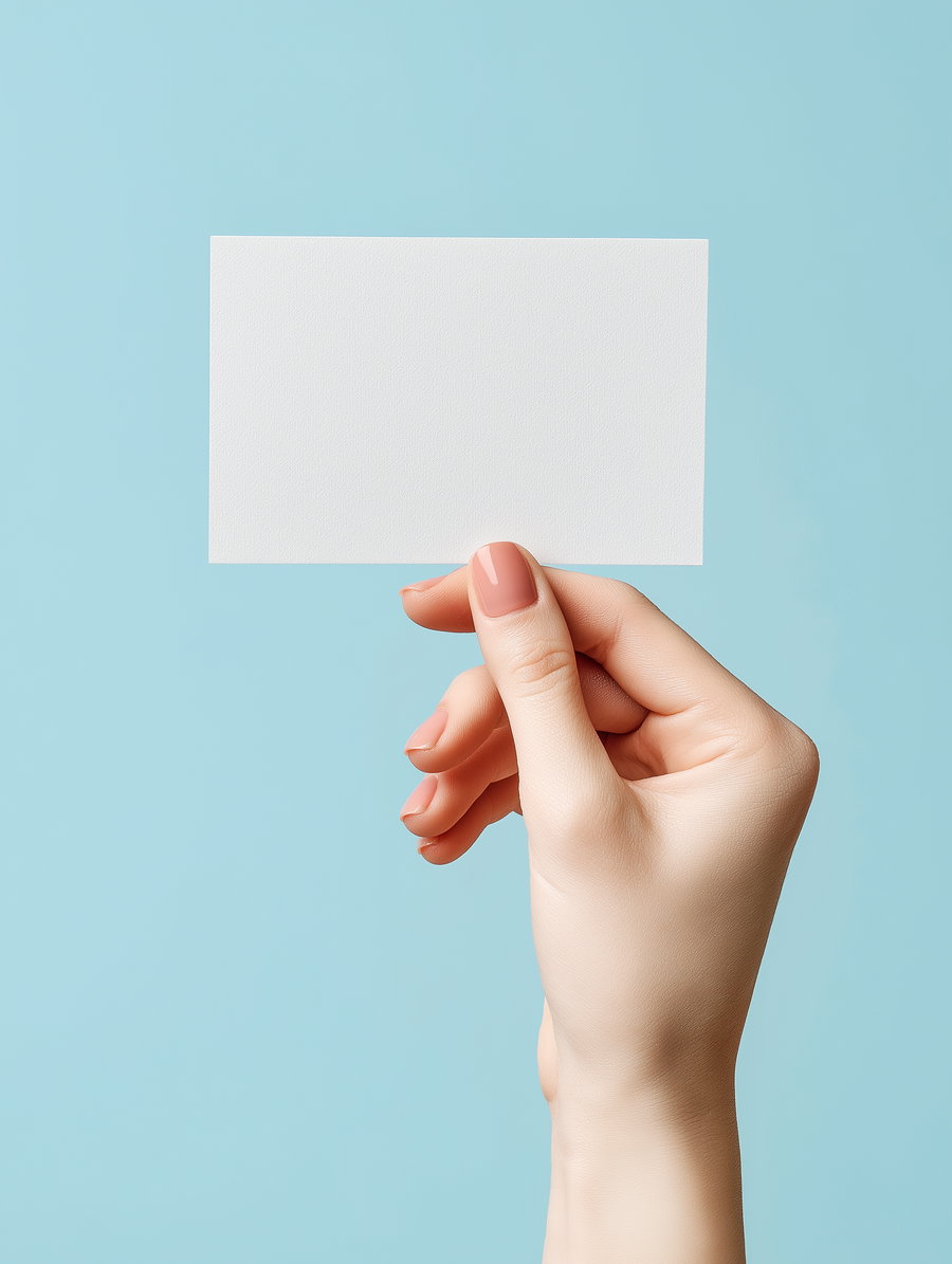 A light-skinned female hand with manicured nails holding a blank white rectangular card on a pale blue background