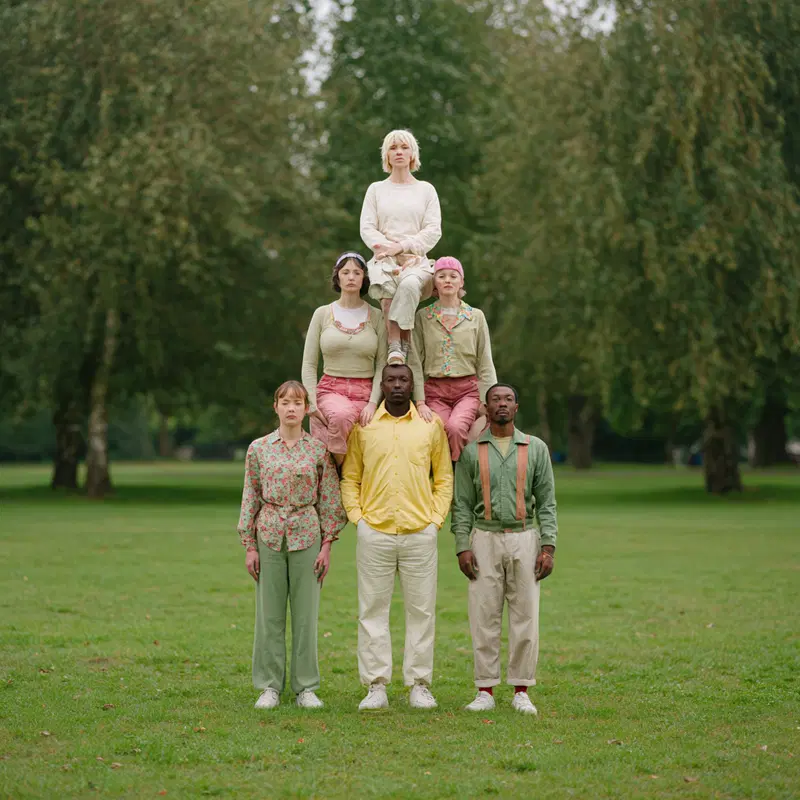 Group of diverse people standing in a human pyramid outdoors with a green forest background