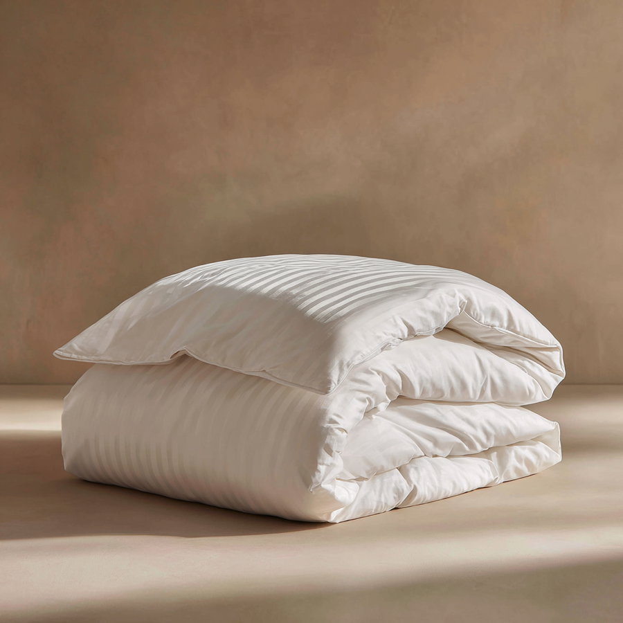 A neatly folded white duvet with subtle vertical stripes placed on a flat beige surface against a plain beige background