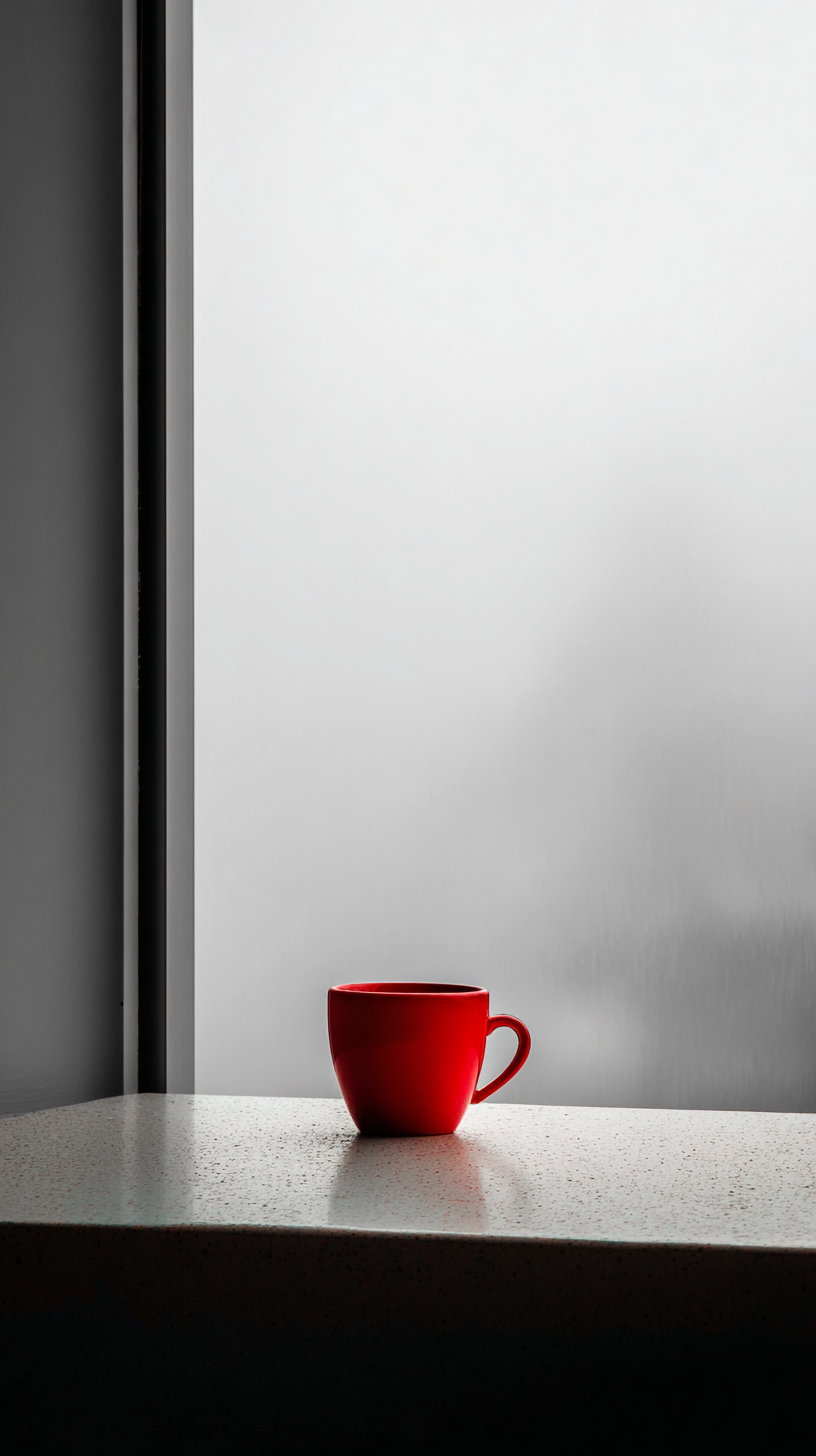 A red coffee cup placed on a speckled countertop with a plain, softly lit background