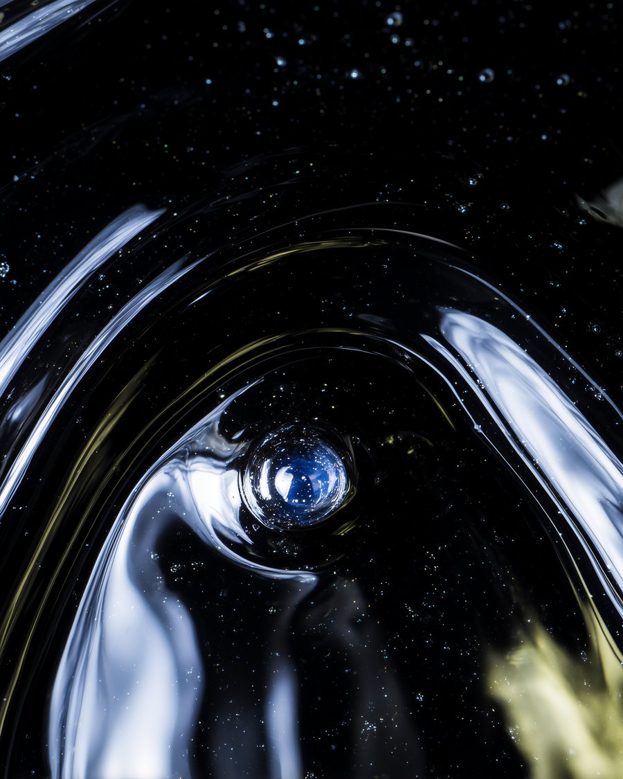 A close-up view of an abstract pattern featuring light reflections, small particles resembling stars, and fluid-like shapes against a dark background.